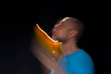 Mavi gömlekli kel adamın sanatsal portresi yanan sarı mumla hareket bulanıklığı yaratıyor. Hafif patika. Siyah arkaplan.