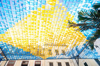 Haziran şenliklerini süsleyen renkli afişler. Plastik nesneler yukarıda asılı. Pelourinho, Brezilya.