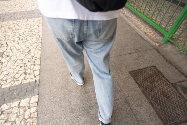 Kaldırımda yürüyen, beyaz gömlek ve kot pantolon giyen bir insanın vücudunun yarısı. Sokaktaki insanlar