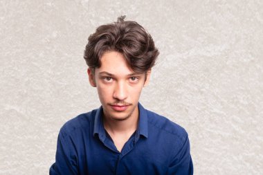 Mavi gömlekli genç ve yakışıklı bir öğrenci kameraya ciddi ciddi bakıyor. Beyaz arka planda izole edilmiş. Kendine güvenen biri. Profesyonel konsept.