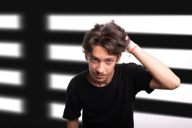 Siyah gömlekli yakışıklı genç adam, gülümsüyor, kameraya bakıyor ve elini saçına sokuyor. Sakin ve mutlu bir insan. Beyaz ırk.