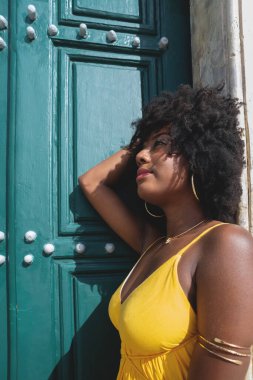 Siyah saçlı, sarı elbiseli güzel bir zenci kadın büyük yeşil kilise kapısına poz veriyor. Mutlu ve gülümsüyor