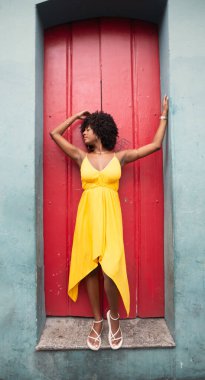 Sarı elbiseli güzel bir kadının uzun bir portresi ve kırmızı bir kapının önünde duran afro saç stili. Kendinden emin ve mutlu biri. Brezilya