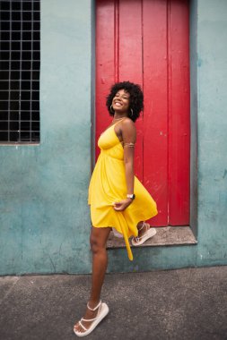 Sarı elbiseli ve kırmızı kapıya doğru yürüyen afro saçlı güzel bir kadının portresi. Kendinden emin ve mutlu biri. Brezilya