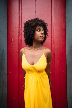Kırmızı kapıya karşı sarı elbiseli ve afro saçlı güzel bir kadının yakın plan portresi. Kendinden emin ve mutlu biri. Brezilya