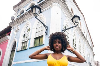 Sarı elbiseli güzel siyah bir kadın ve eski evin arka planında afro saç stili. Kendinden emin ve mutlu biri. Brezilya