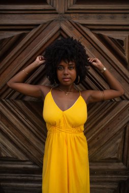 Yüzyıllık ahşap bir kapıya karşı, sarı bir elbise giyen, afro saçlı bir kadının yakın plan portresi. Kendine güvenen biri. Brezilya