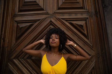 Yüzyıllık ahşap bir kapıya karşı, sarı bir elbise giyen, afro saçlı bir kadının yakın plan portresi. Kendine güvenen biri. Brezilya