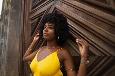 Yüzyıllık ahşap bir kapıya karşı, sarı bir elbise giyen, afro saçlı bir kadının yakın plan portresi. Kendine güvenen biri. Brezilya