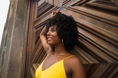 Yüzyıllık ahşap bir kapıya karşı, sarı bir elbise giyen, afro saçlı bir kadının yakın plan portresi. Kendine güvenen biri. Brezilya