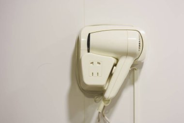 Banyonun duvarında beyaz otel saç kurutma makinesi asılı..