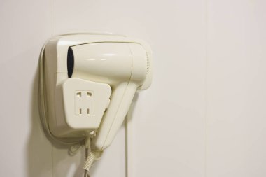 Banyonun duvarında beyaz otel saç kurutma makinesi asılı..