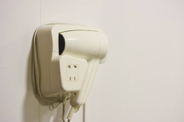 Banyonun duvarında beyaz otel saç kurutma makinesi asılı..