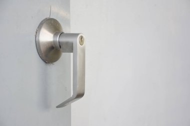 Kapı koluna yakın çekim. Kapı kolu metalden yapılmış ve modern, parlak bir tasarımı var. Kapı kolu kapıya bağlı ve pürüzsüz, açık renkli bir maddeden yapılmış gibi görünüyor..