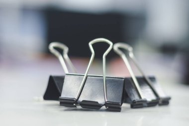 Beyaz bir yüzeyde sıralanmış birkaç siyah klasör klibinin yakın plan görüntüsü. Klasör klipsleri siyah üçgen gövdeli ve gümüş saplı metalik.. 