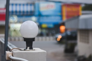 Beton bir direğe monte edilmiş küresel bir açık hava lambasının yakın plan görüntüsü. Aydınlatma armatüründe buzlu cam bir küre ve siyah bir baz var. Posta direğinin tabanına bağlı bir elektrik kanalı var..