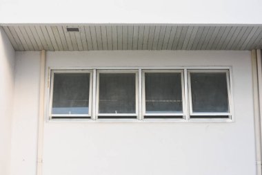 Binanın dış duvarının yatay olarak sıralanmış dört dikdörtgen pencereli kısmı. Pencereler beyaz çerçeveli ve biraz kirli ya da sisli görünüyor..