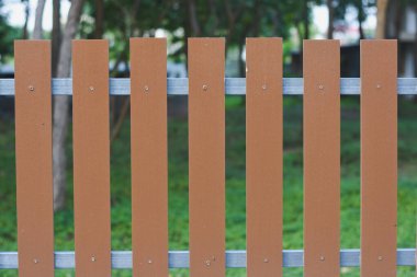 Yatay metal çubuklara sabitlenmiş dikey kahverengi tahta çıtçıtlardan oluşan çitin bir bölümü. Tahta çıtalar eşit aralıklarla ve vidalarla metal parmaklıklara sabitlenmiş.. 