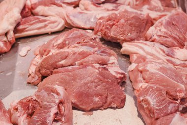 Metalik bir yüzeye yerleştirilmiş birkaç parça çiğ domuz eti. Et taze görünüyor, yağ ve kas dokusundan oluşan görünür bir mermer. Parçalar şekil ve boyut olarak değişir..