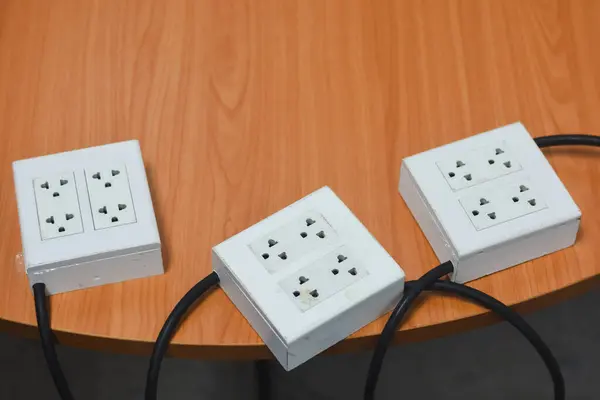 Tahta bir yüzeye yerleştirilmiş üç beyaz elektrik şeridi. Her güç şeridi, birden fazla tür prizin eklenmesine olanak sağlayan iki çift evrensel sokete sahiptir..