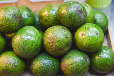 Avokadolar yeşil, bazı kahverengi noktalar ve ciltlerinde pürüzlü lekeler var. Muhtemelen bir market veya mağaza vitrininde birbirine yakın dizilmiş durumdalar..