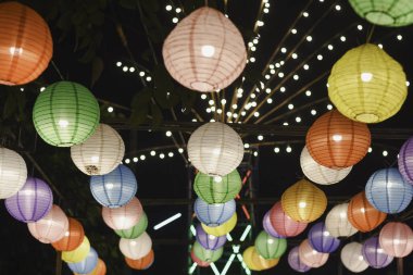 Yukarıdan sarkan renkli kağıt fener koleksiyonu karanlık bir gece gökyüzüne karşı aydınlatılıyor.. 