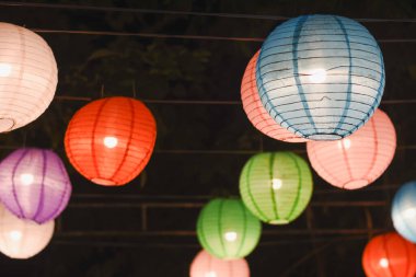 Yukarıdan sarkan renkli kağıt fener koleksiyonu karanlık bir gece gökyüzüne karşı aydınlatılıyor.. 