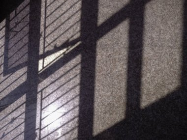 Döşeme üzerine parmaklıklar düşmüş bir pencerenin gölgesini gösterir. Gölgeler yerde ızgara benzeri bir desen oluşturuyor. Güneş ışığı karoların bazı parçalarını aydınlatıyor..