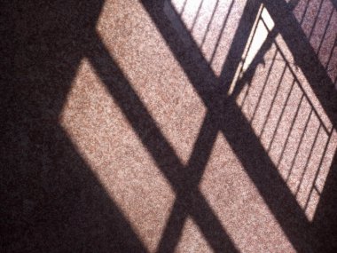 Döşeme üzerine parmaklıklar düşmüş bir pencerenin gölgesini gösterir. Gölgeler yerde ızgara benzeri bir desen oluşturuyor. Güneş ışığı karoların bazı parçalarını aydınlatıyor..