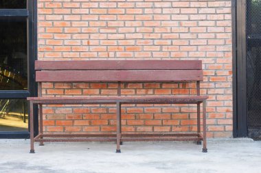 Duvara dayanmış metal çerçeveli ahşap bir bank. Yedek kulübesinde iki yatay ahşap tahta ve tek bir ahşaptan yapılmış bir koltuk var..