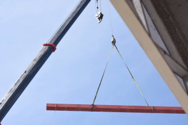 Bir vincin üst kısmı açık mavi gökyüzüne karşı. Turnanın kolu çapraz olarak uzatılmış ve bir kanca vincin kablosunun ucunda asılı..