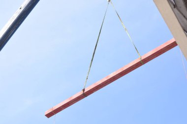 Bir vincin üst kısmı açık mavi gökyüzüne karşı. Turnanın kolu çapraz olarak uzatılmış ve bir kanca vincin kablosunun ucunda asılı..