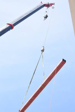 Bir vincin üst kısmı açık mavi gökyüzüne karşı. Turnanın kolu çapraz olarak uzatılmış ve bir kanca vincin kablosunun ucunda asılı..