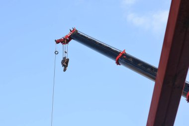 Bir vincin üst kısmı açık mavi gökyüzüne karşı. Turnanın kolu çapraz olarak uzatılmış ve bir kanca vincin kablosunun ucunda asılı..