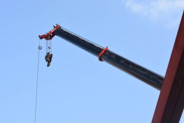 Bir vincin üst kısmı açık mavi gökyüzüne karşı. Turnanın kolu çapraz olarak uzatılmış ve bir kanca vincin kablosunun ucunda asılı..