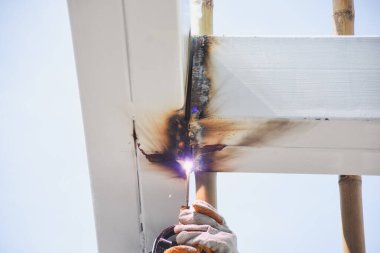 Beyaz boyanmış metal bir yapının köşesindeki kaynak işlemi. Yapının köşesindeki kaynaklardan kıvılcımlar ve duman görülebiliyor. Kaynak bölgesinde yanık izleri ve is lekeleri var..