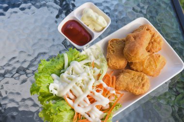 Tabakta birkaç altın-kahverengi kızarmış tavuk nugget, yanında maruldan oluşan taze salata ve beyaz bir sos serpiştirilmiş lahana bulunuyor.. 