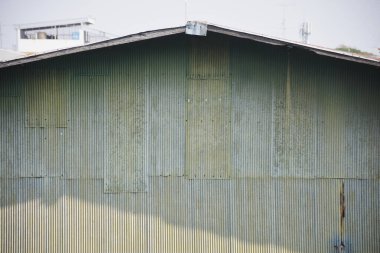 Bükülmüş metal bir binanın yan tarafında. Binanın duvarı, bazı bölgelerde yıpranmış ve hafifçe paslanmış gibi görünen dikey kıvrımlı metal levhalardan oluşuyor..