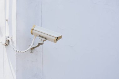 Güvenlik kamerası bir binanın dış duvarına monte edilmiş. Kamera koruyucu bir kılıfın içinde ve duvara metal bir desteyle tutturulmuş..