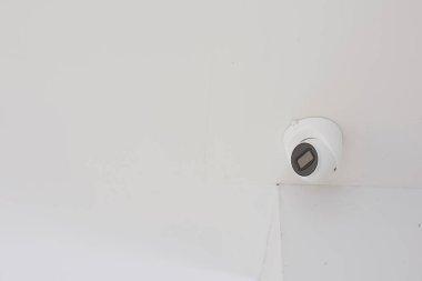 Beyaz kubbe güvenlik kamerası beyaz bir tavana monte edilmiş. Kameranın siyah bir mercek alanı var ve tavanın köşesine yerleştirilmiş..