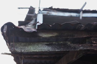 Kötüleşen bir çatı yapısının yakın plan görüntüsü. Çatı eğri büğrü ve paslı metal levhalardan yapılmıştır.. 