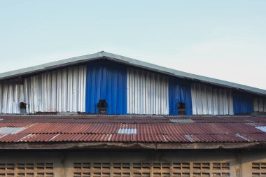 Ahşap kaplamalı iki katlı bir bina. Üst katta açık mavi ahşap duvarlar var. Ortasında dikey metal parmaklıklar var. Muhtemelen bir pencere ya da balkon alanı var..