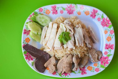 Pirinç yatağında düzgünce sıralanmış tavuk göğsü dilimleri var. Tavukla pirincin etrafında salatalık dilimleri, ciğer parçaları ve diğer organları görebilirsiniz..