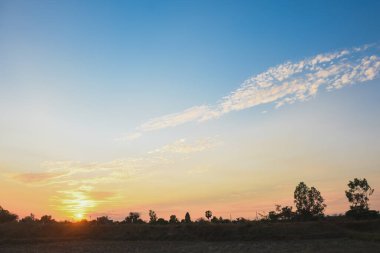 Gün batımının huzurlu ve huzurlu anı. Güneş 'in ılık turuncu ve sarı renkleri ufuk boyunca yayıldı. Derin mavi gökyüzünde kusursuz bir şekilde harmanlandı..