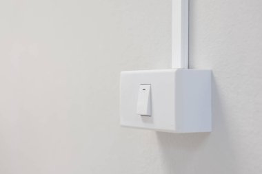 Beyaz bir duvara monte edilmiş beyaz bir ışık düğmesi gösteriyor. Düğme dikdörtgen ve üst tarafında yatay bir çizgi var. Bu da düğmenin konumunu gösteriyor..