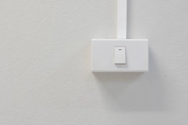 Beyaz bir duvara monte edilmiş beyaz bir ışık düğmesi gösteriyor. Düğme dikdörtgen ve üst tarafında yatay bir çizgi var. Bu da düğmenin konumunu gösteriyor..