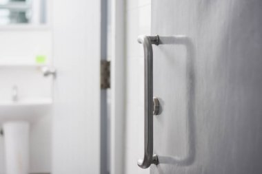 Kapı kolu kapıya bağlı. Sapı metalik ve kıvrımlı bir tasarımı var. Kapı biraz aralıkmış. Arka plandaki banyo iç kısmından belli oluyor..