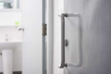 Kapı kolu kapıya bağlı. Sapı metalik ve kıvrımlı bir tasarımı var. Kapı biraz aralıkmış. Arka plandaki banyo iç kısmından belli oluyor..