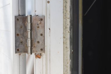 Beyaz bir kapı çerçevesine asılmış bir kapı menteşesi. Menteşe metalik ve kapıya ve çerçeveye tutturan birden fazla vidası var..