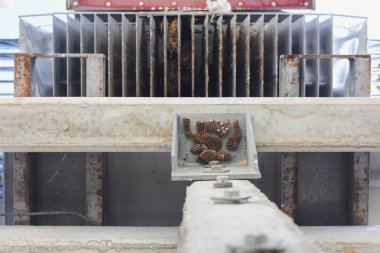 Mekanik bir yapı, muhtemelen endüstriyel makinelerin bir parçası. Ana odak noktası, beton kirişe bağlı metal bir plaka ve üzerinde bal peteği benzeri yapılar var.. 